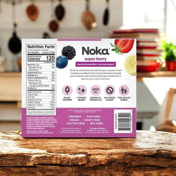 A box of Noka Organic Super Berry Smoothies, 12-count, rests on a wooden kitchen counter with nutrition facts and features like plant protein and vitamin blend. It's perfectly plant-based and suitable for adults and kids.