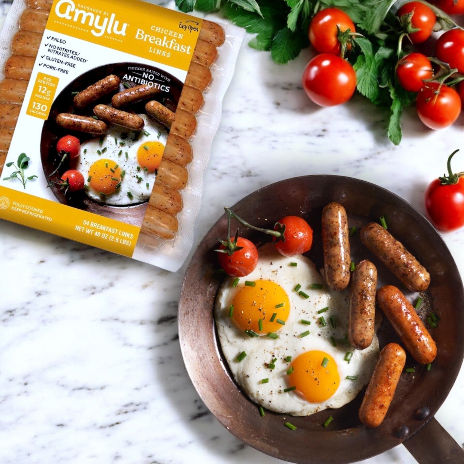 Amylu Chicken Breakfast Sausage Links (2.5 lbs) are pictured with a skillet of cooked links, two sunny-side-up eggs, cherry tomatoes, and herbs on marble, making a tempting start to your high-protein breakfast.