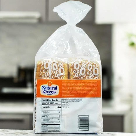 A 3-count pack of Natural Oven's Keto Friendly Bread in a clear plastic bag with an orange label is on a kitchen counter, displaying the nutrition facts on the back.