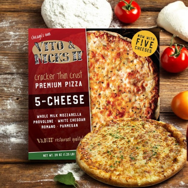 A package of Vito & Nick's II Cracker Thin Crust 5-Cheese Pizza, 20 oz, rests beside a baked pizza adorned with a Five-Cheese Blend, surrounded by tomatoes, garlic, and flour on wood—capturing the essence of Chicago Tavern-Style Pizza with its signature cracker thin crust.