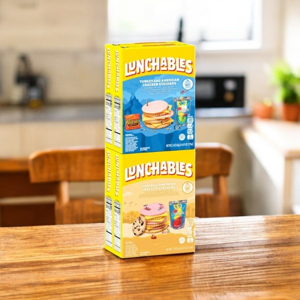 Two boxes of Lunchables Cracker Stackers, Ham and Turkey Variety Pack (4 count), are stacked on a wooden kitchen table, ready to be packed into school lunches for a fun and tasty meal.