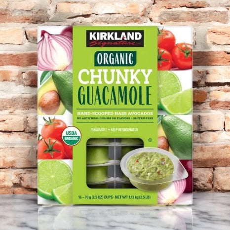 A box of Kirkland Signature Organic Chunky Guacamole-16 Count displays vibrant avocados, lime, tomatoes, and onion images on a stone background with a tasty serving suggestion for the perfect avocado dip.