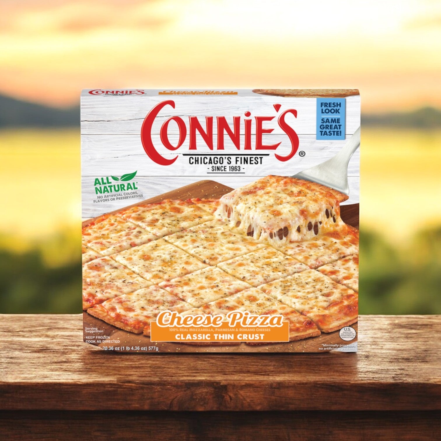 A box of Connie's Pizza Classic Thin Crust Cheese, 20.36 oz., sits on a wooden table against a blurred outdoor backdrop, offering an effortless gourmet baking experience!.