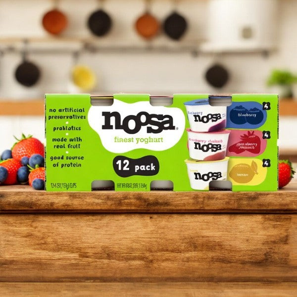 A Noosa Yoghurt Variety Pack, 12 oz, 4-count, sits on a wooden surface, featuring blueberry, strawberry rhubarb, and lemon flavors. This creamy probiotic snack is packed with real fruit and provides 6g of protein.