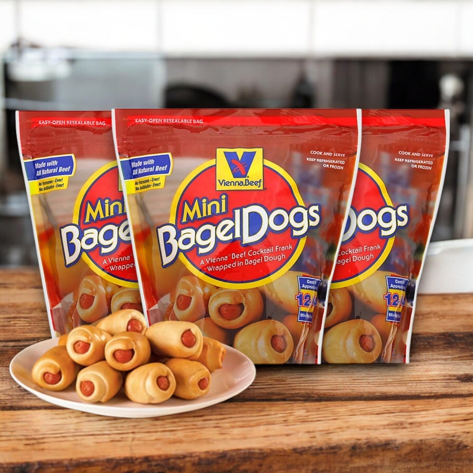 Three packs of Vienna Beef Natural Mini Bagel Dogs (12 oz. each, with 36 total mini dogs) are shown behind a wooden plate of cooked mini bagel dogs. The packaging emphasizes "all natural beef" and the choice to "microwave or oven bake." Kid-friendly family favorite delight!.