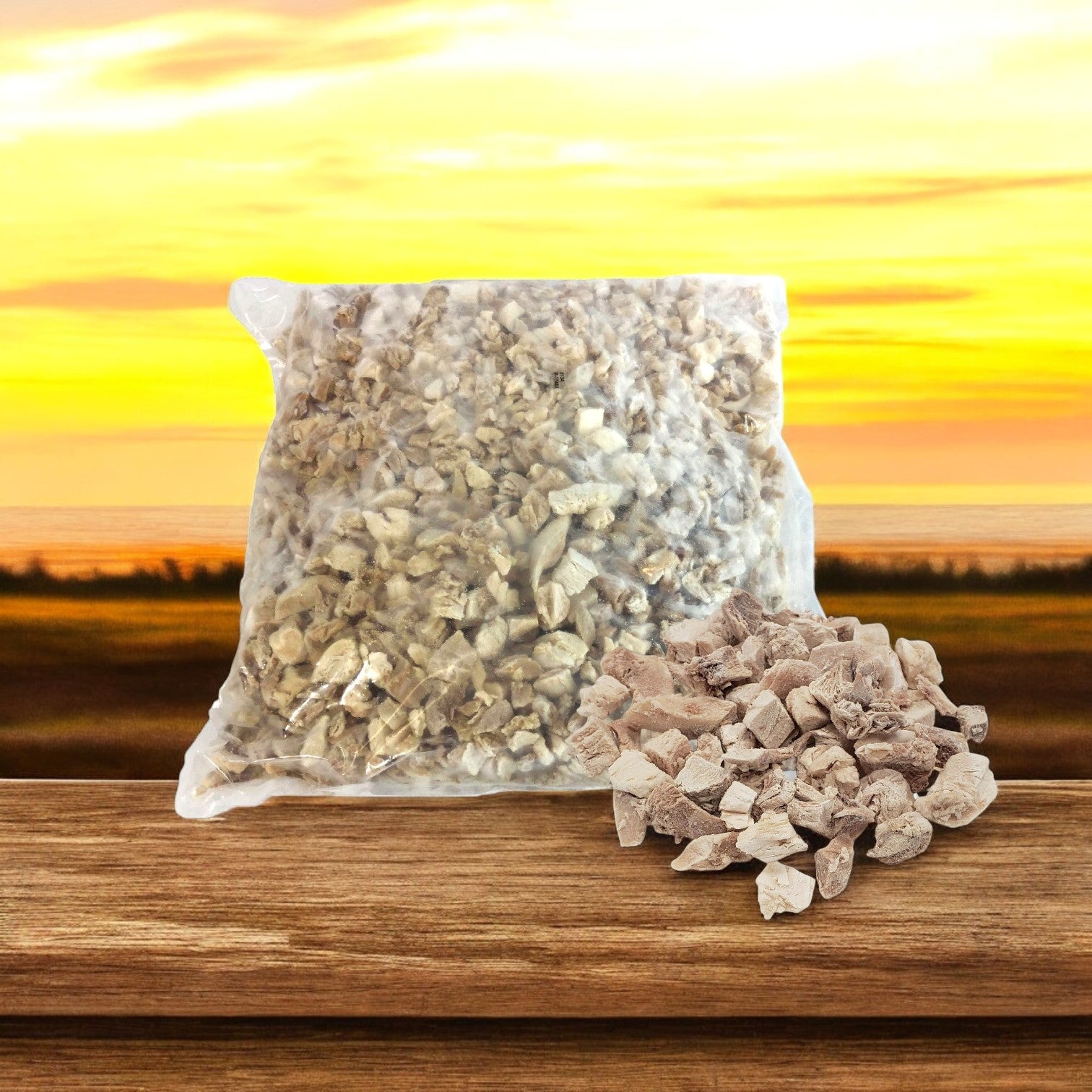 A bag with small, light brown rocks lies on a wooden surface, loose rocks scattered in front. A sunset landscape forms the backdrop, reminiscent of a cozy kitchen where Sysco Classic Diced Chicken Meat, 0.5 Inch Dark & White from Sysco could be prepared and enjoyed.