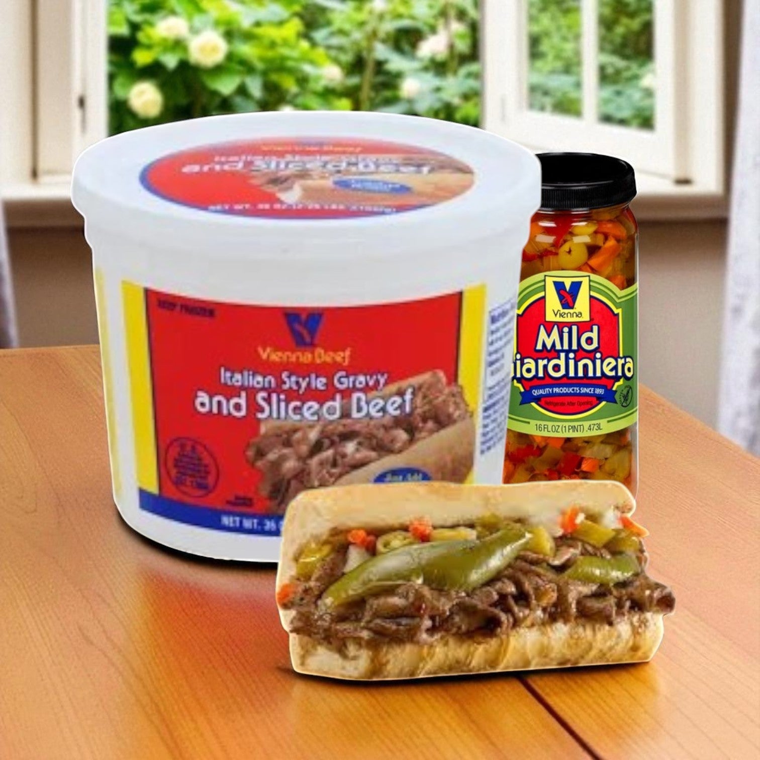 A 36 oz. container of Vienna Beef Italian Style Gravy and Sliced Beef, a jar of mild giardiniera, and a beef sandwich are on a table with a window in the background.