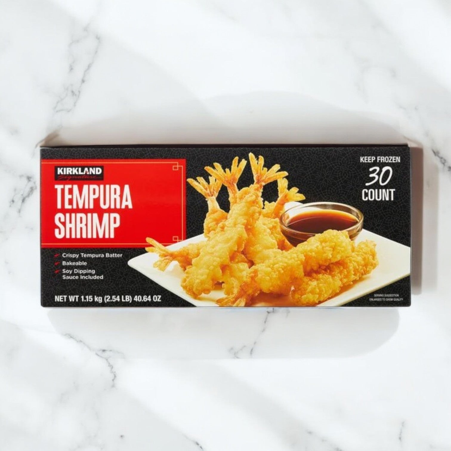 A box of Kirkland Signature Tempura Shrimp, 2.35 lbs, 30-count (3 packs), is shown on a marble surface with a picture of crispy tempura shrimp and dipping sauce on the packaging.