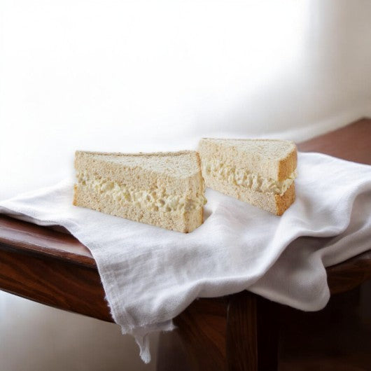 Two halves of an E.A. Sween Albacore Tuna Salad Sandwich rest on a white cloth atop a wooden table.