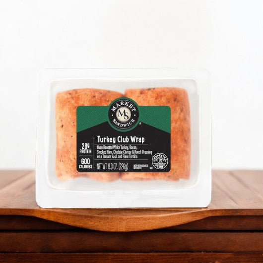 E.A. Sween's Turkey Club Wrap with Bacon, Ham, Cheddar Cheese, and Ranch Dressing is displayed on a wooden surface. The wrap ships frozen and boasts 29g protein and 600 calories for a satisfying crunch. Shelf life is 30 days in the cooler once thawed.