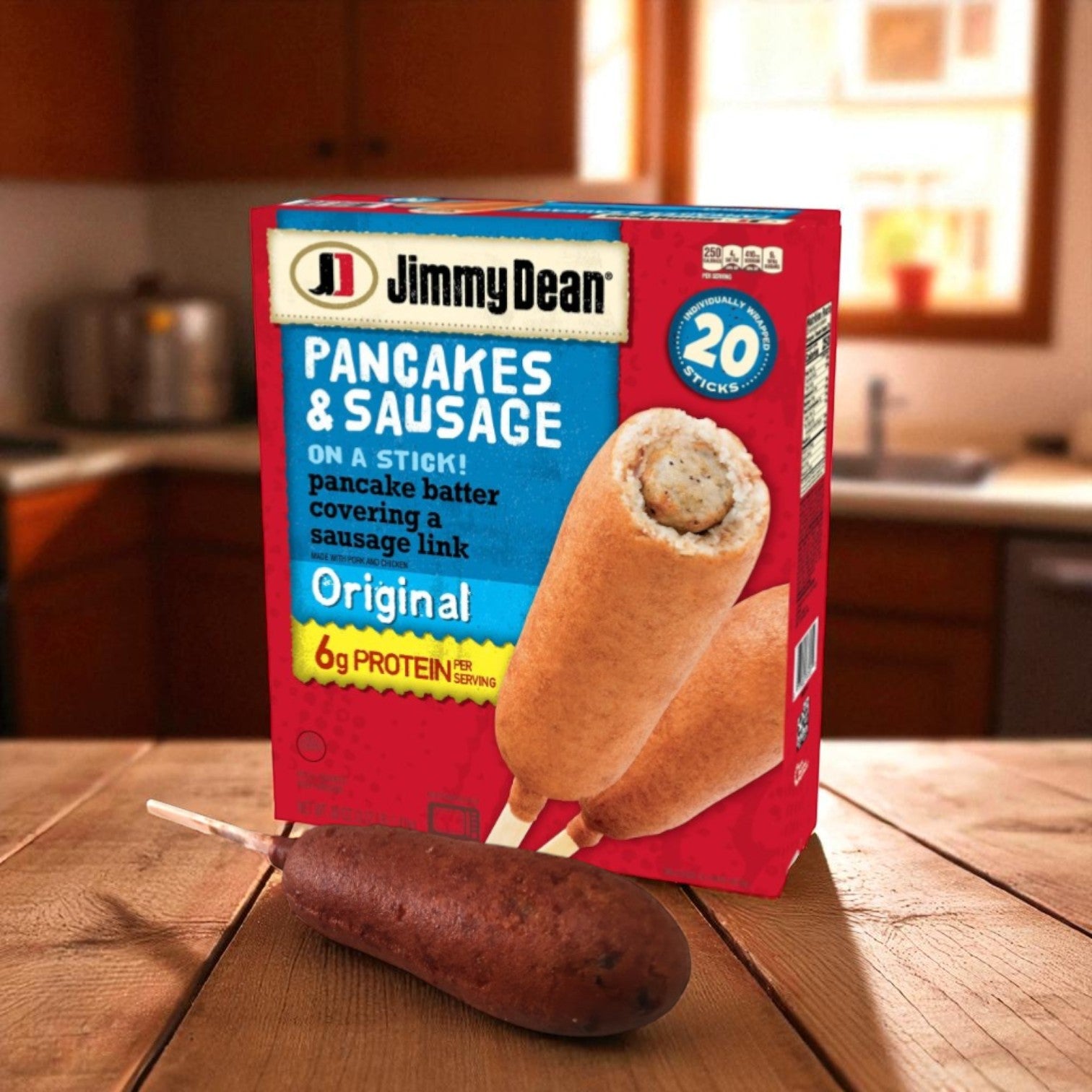 A box of Jimmy Dean Original Pancake and Sausage on a Stick, Frozen, 20 ct-1 Pack rests on a wooden table with one ready-to-eat treat in front, showcasing this popular Jimmy Dean breakfast option. A cozy kitchen is visible in the background.